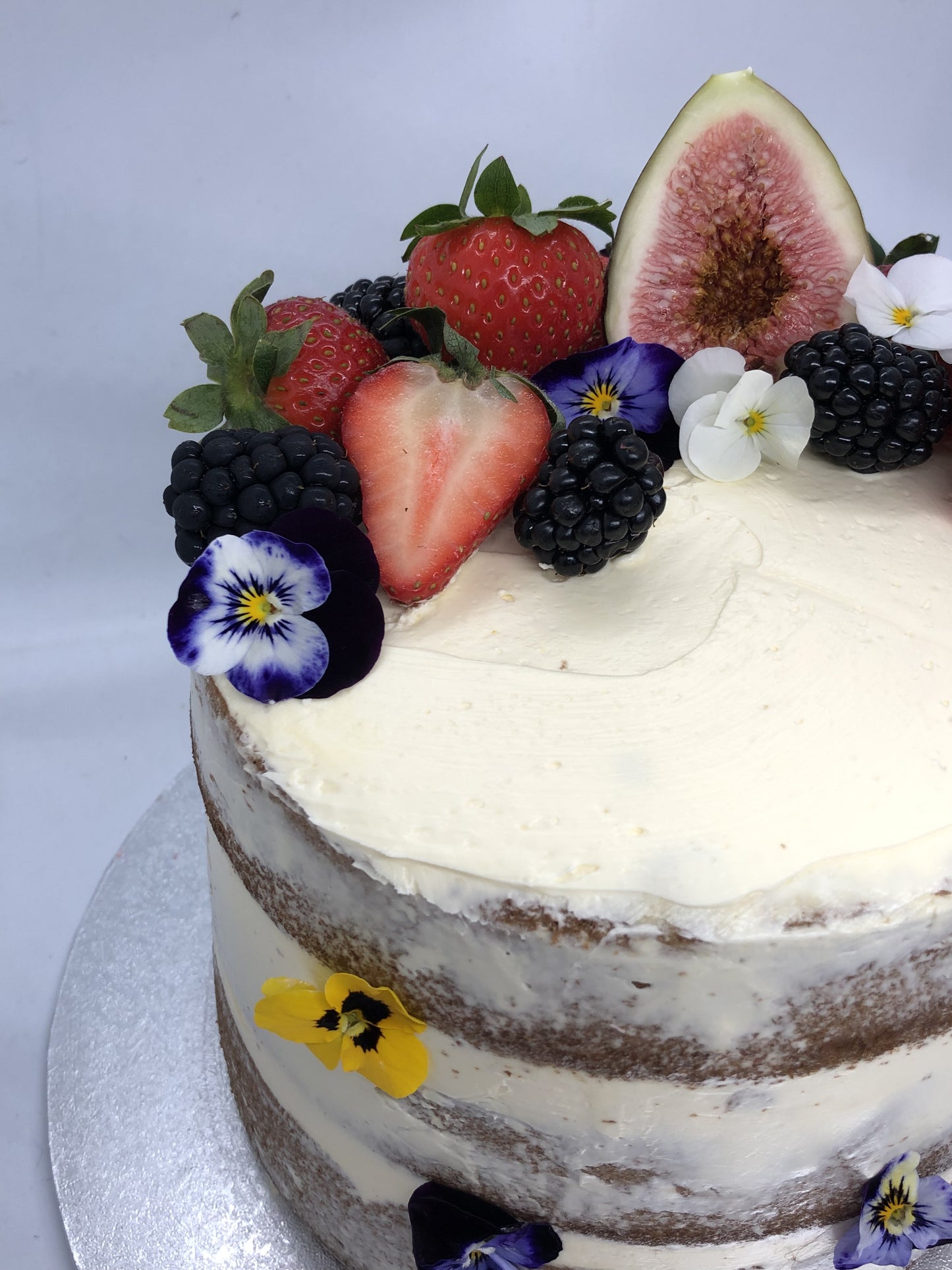Naked cake with fruits and edible flowers on side